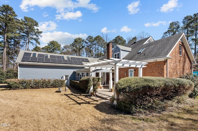 rear view of house featuring brick siding, a yard, a chimney, solar panels, and a pergola