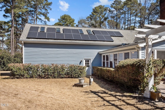 rear view of house with solar panels, a yard, and roof with shingles