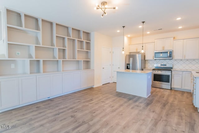 kitchen featuring stainless steel appliances, a kitchen island, light wood-type flooring, tasteful backsplash, and decorative light fixtures