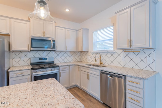 kitchen with stainless steel appliances, wood finished floors, a sink, and light stone counters