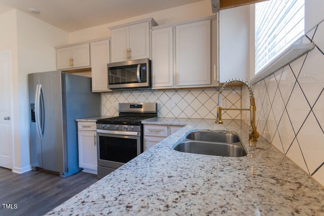 kitchen featuring dark wood-style flooring, appliances with stainless steel finishes, light stone counters, and a sink