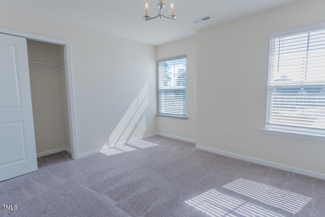 unfurnished bedroom with baseboards, visible vents, a notable chandelier, and carpet flooring