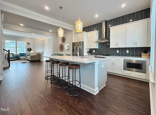 kitchen with open floor plan, decorative light fixtures, stainless steel appliances, wall chimney range hood, and white cabinetry