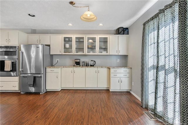 kitchen with dark wood-style flooring, white cabinets, appliances with stainless steel finishes, glass insert cabinets, and pendant lighting