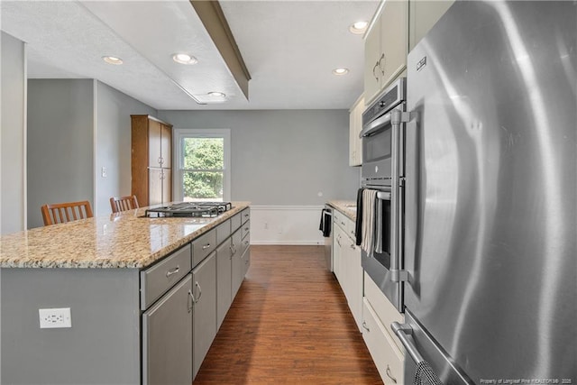 kitchen featuring a breakfast bar area, gray cabinetry, dark wood-style flooring, a kitchen island, and appliances with stainless steel finishes