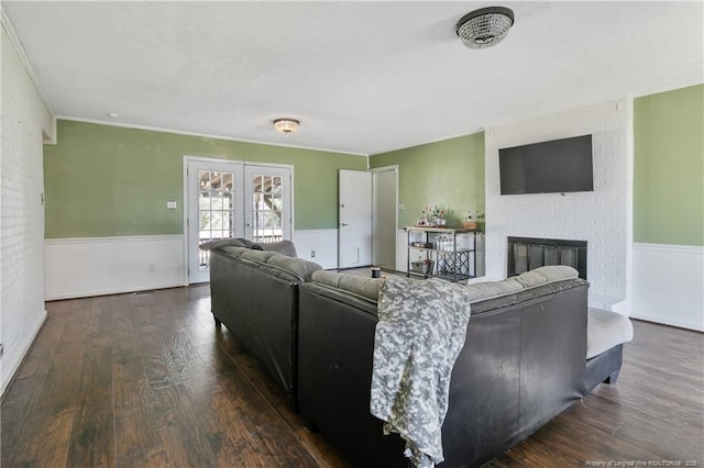 living room with french doors, wainscoting, dark wood finished floors, and a brick fireplace