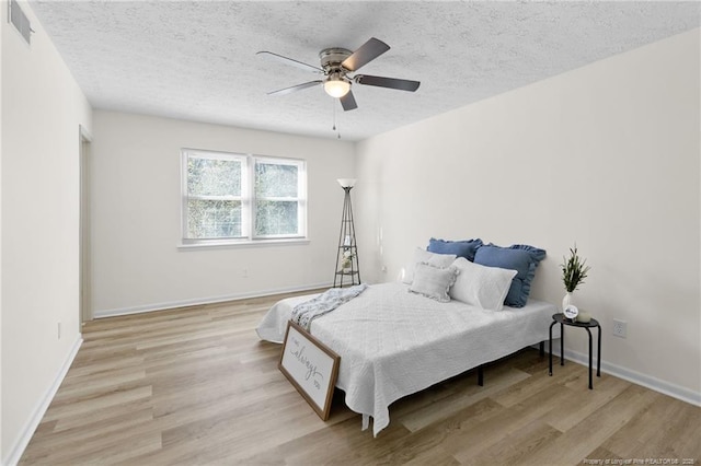 bedroom featuring a textured ceiling, a ceiling fan, visible vents, and light wood-style floors