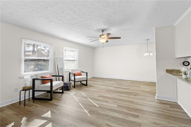 living area featuring light wood-style floors, a textured ceiling, baseboards, and a ceiling fan