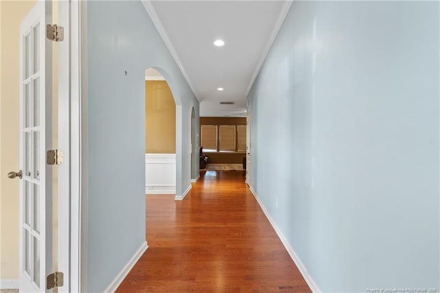 hallway featuring arched walkways, recessed lighting, wood finished floors, baseboards, and ornamental molding