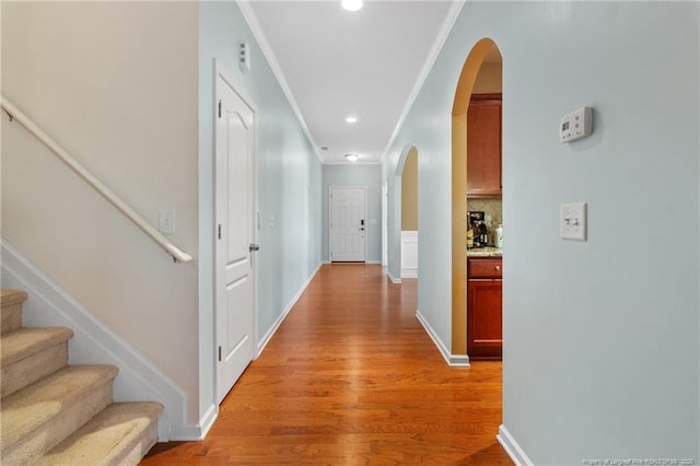 corridor with light wood finished floors, baseboards, arched walkways, stairway, and ornamental molding