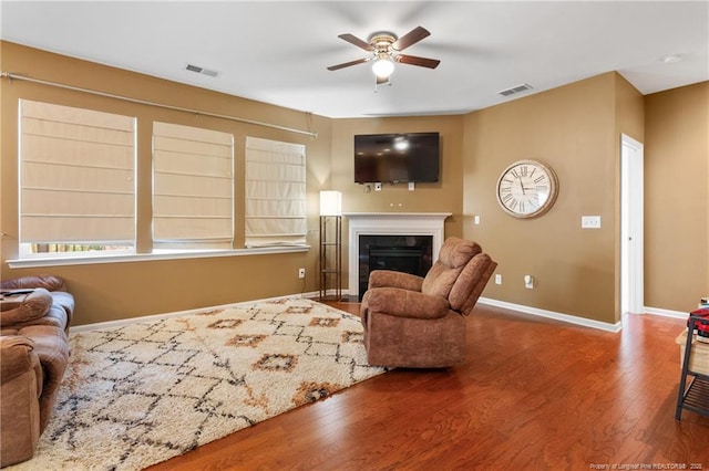 living area with a fireplace with flush hearth, visible vents, baseboards, and wood finished floors