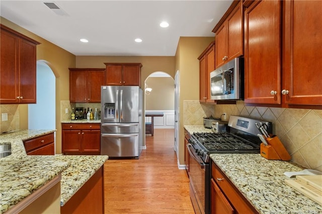 kitchen featuring visible vents, arched walkways, light wood-style flooring, light stone counters, and stainless steel appliances