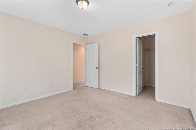 unfurnished bedroom featuring a closet, visible vents, a spacious closet, light carpet, and baseboards