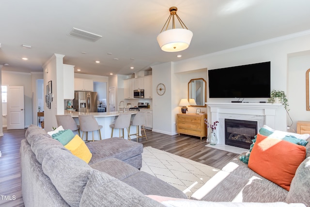 living room with dark wood-style floors, recessed lighting, visible vents, ornamental molding, and a fireplace with flush hearth