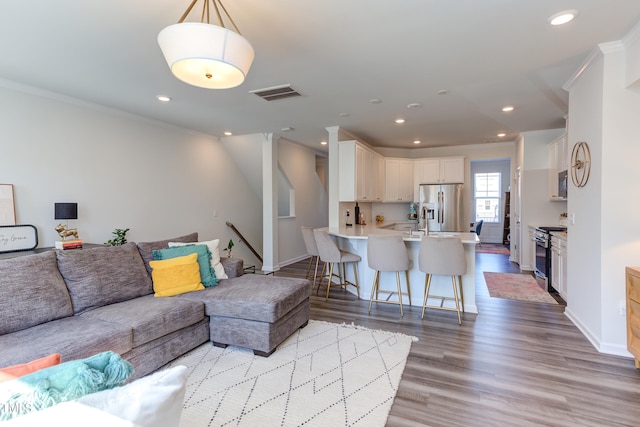 living room featuring light wood-style flooring, recessed lighting, visible vents, and crown molding