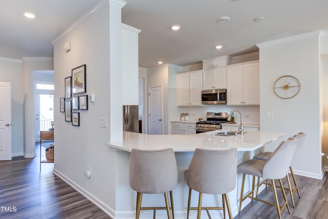 kitchen featuring stainless steel appliances, light countertops, a sink, a peninsula, and a kitchen bar