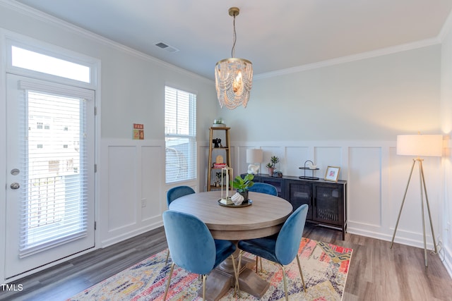 dining space with visible vents, dark wood-style floors, a wainscoted wall, crown molding, and a chandelier