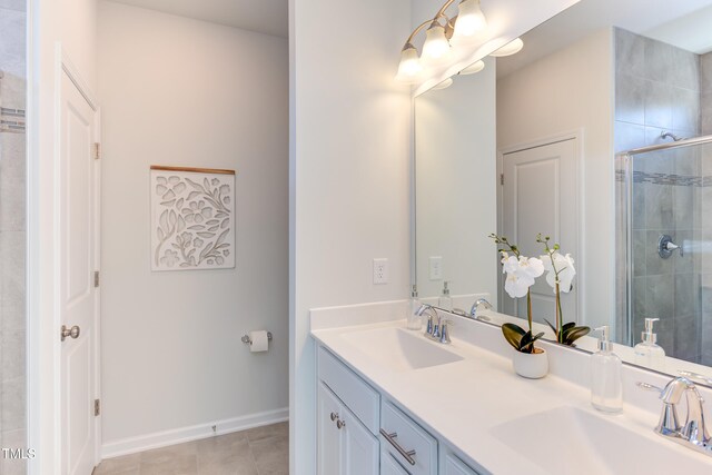 full bath with a sink, a shower stall, baseboards, and double vanity