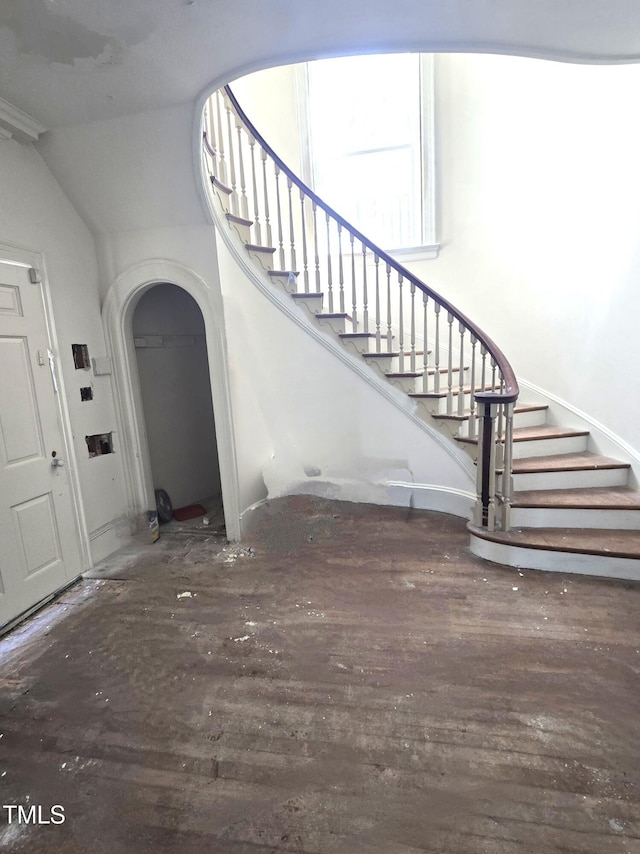 entryway featuring arched walkways, stairway, and dark wood-style floors