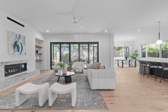 living room featuring built in shelves, recessed lighting, light wood-style flooring, a ceiling fan, and a high end fireplace