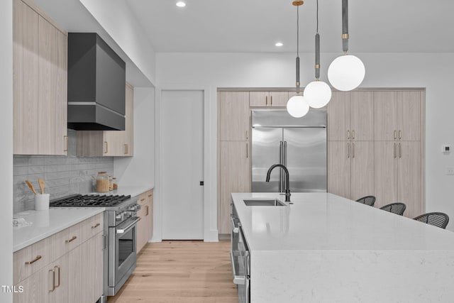 kitchen with premium appliances, pendant lighting, light brown cabinetry, a sink, and an island with sink