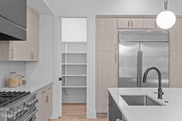 kitchen featuring light brown cabinets, light wood-style flooring, a sink, stainless steel built in fridge, and pendant lighting