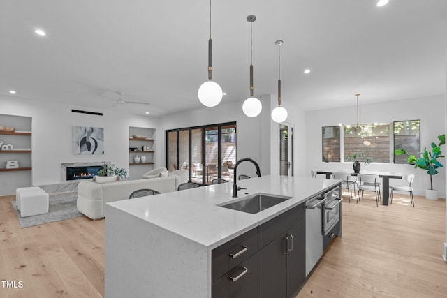 kitchen featuring a kitchen island with sink, a sink, hanging light fixtures, light wood-type flooring, and modern cabinets