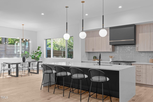 kitchen with light brown cabinetry, wall chimney range hood, modern cabinets, and pendant lighting