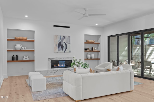 living area featuring light wood finished floors, built in shelves, a premium fireplace, and visible vents