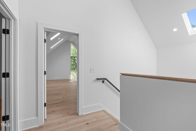 hall with recessed lighting, light wood-style flooring, an upstairs landing, vaulted ceiling with skylight, and baseboards