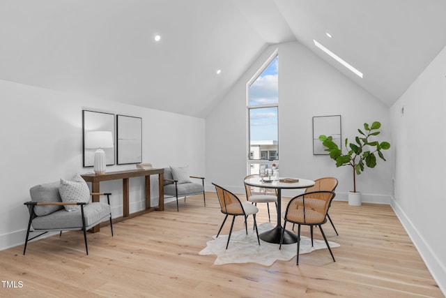 dining room with light wood-style floors, a skylight, high vaulted ceiling, and baseboards