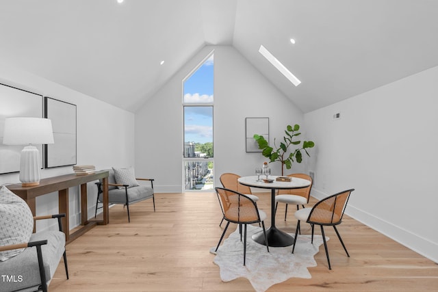 dining room with light wood-style floors, a skylight, high vaulted ceiling, and baseboards