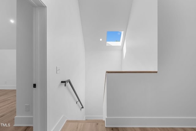 stairway with a skylight, baseboards, and wood finished floors