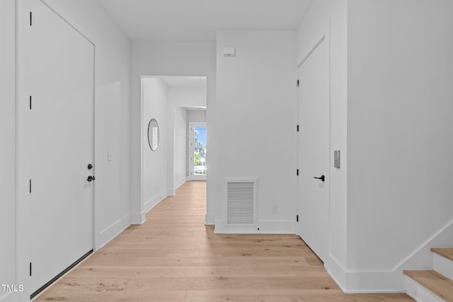 hallway with light wood-style floors, baseboards, stairs, and visible vents