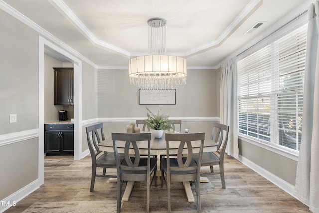 dining space featuring a chandelier, light wood-type flooring, a raised ceiling, and crown molding