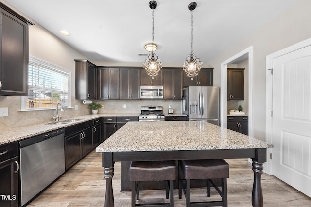 kitchen with a breakfast bar area, a sink, a kitchen island, appliances with stainless steel finishes, and pendant lighting