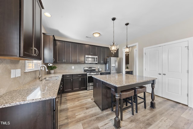 kitchen featuring a center island, decorative light fixtures, appliances with stainless steel finishes, a sink, and light stone countertops