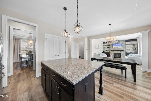 kitchen featuring a fireplace, light wood finished floors, a kitchen island, dark brown cabinets, and light stone countertops