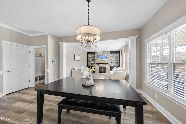 dining area featuring a notable chandelier, ornamental molding, a stone fireplace, wood finished floors, and baseboards