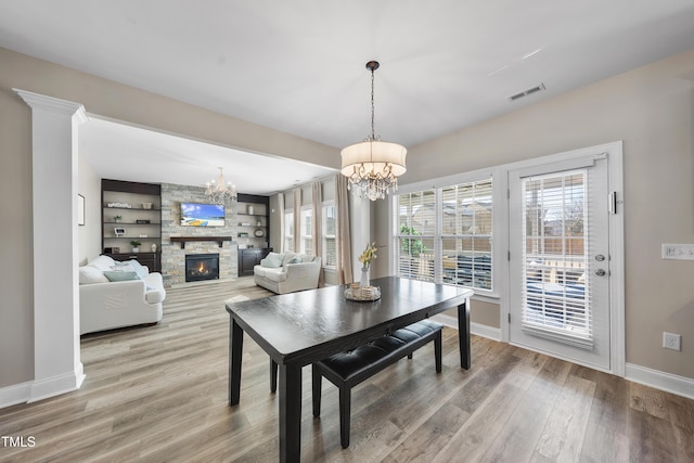 dining area with a fireplace, wood finished floors, visible vents, and an inviting chandelier