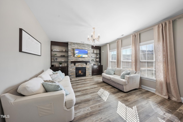 living room featuring a stone fireplace, built in shelves, wood finished floors, and an inviting chandelier