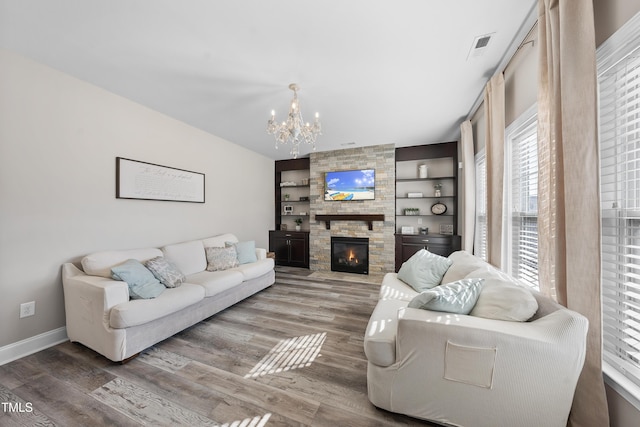 living area featuring a stone fireplace, wood finished floors, visible vents, and a notable chandelier