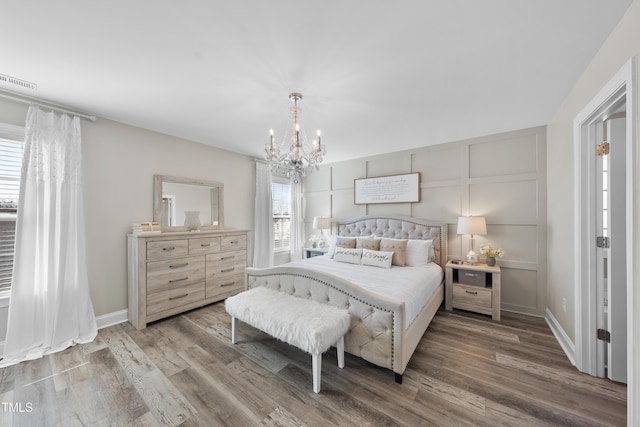 bedroom featuring a chandelier, a decorative wall, wood finished floors, visible vents, and baseboards