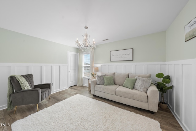 living room with a wainscoted wall, a notable chandelier, visible vents, a decorative wall, and wood finished floors