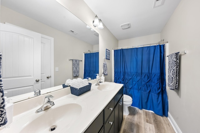 full bath featuring double vanity, visible vents, toilet, a sink, and wood finished floors