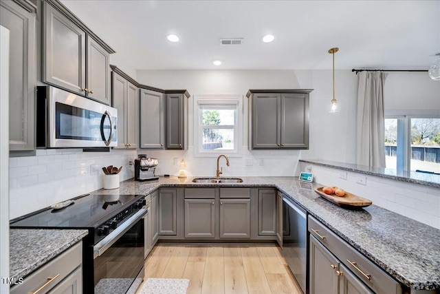 kitchen with gray cabinetry, a peninsula, a sink, appliances with stainless steel finishes, and decorative light fixtures