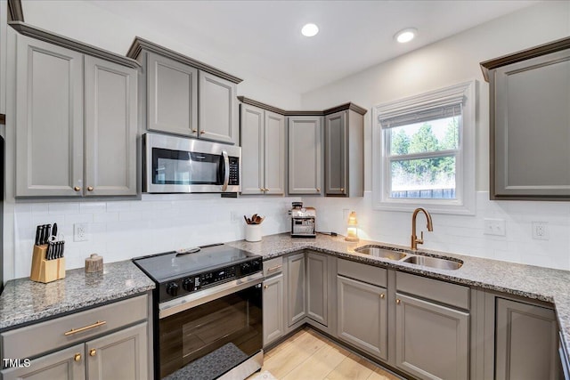 kitchen featuring light stone counters, gray cabinets, stainless steel microwave, electric range oven, and a sink