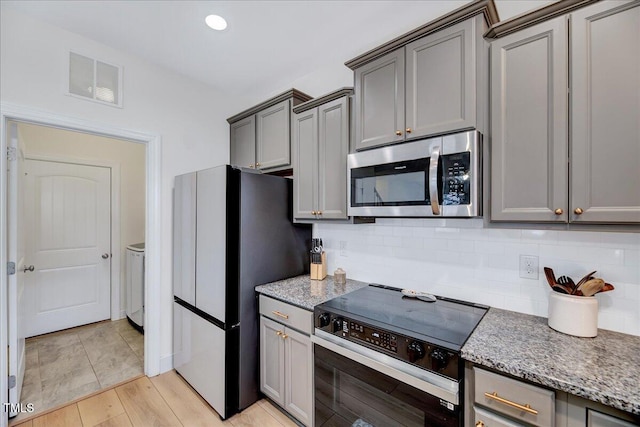 kitchen with visible vents, decorative backsplash, stainless steel microwave, freestanding refrigerator, and range with electric stovetop