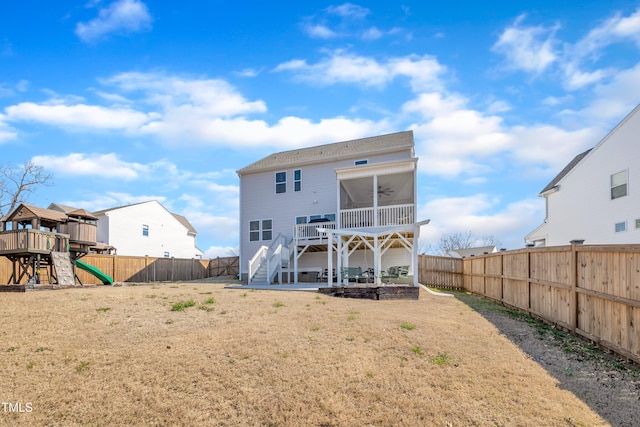 rear view of property with ceiling fan, a playground, a fenced backyard, stairway, and a lawn