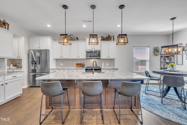 kitchen with stainless steel appliances, visible vents, a kitchen island with sink, white cabinets, and wood finished floors